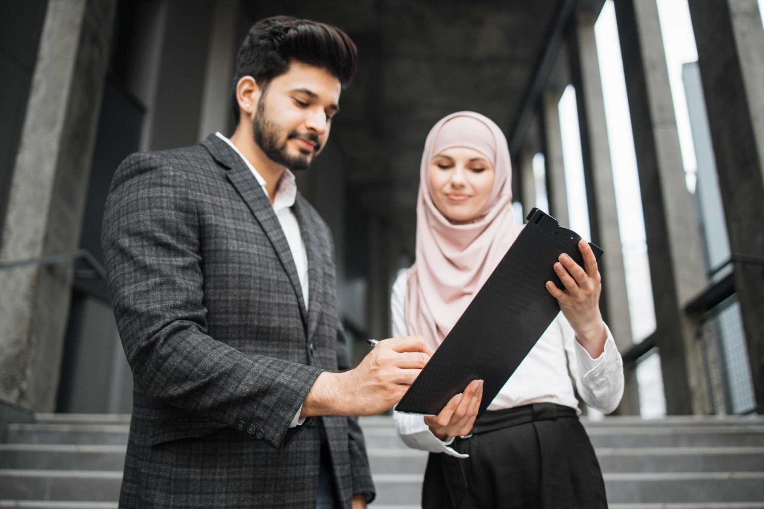 woman-in-hijab-holding-clipboard-while-man-signing-XZYLMHE.jpg
